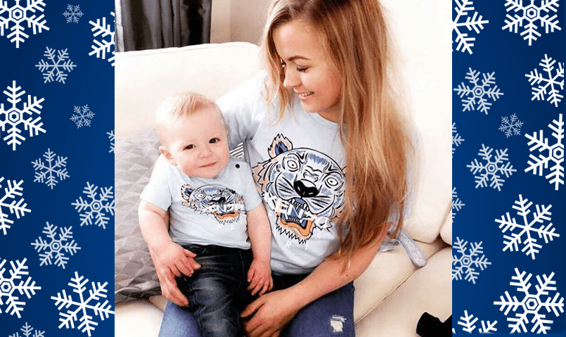 Rhiannon sits in living room with one year old Ollie on her knee. Both wear jeans and matching t-shirts.