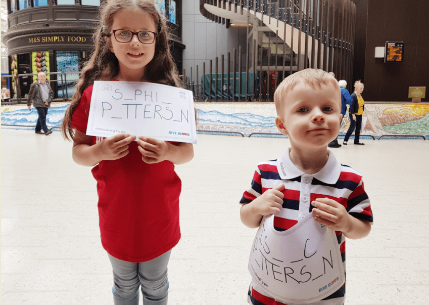 Sophia and Isaac smile as they hold up posters of their names missing vital letters.  