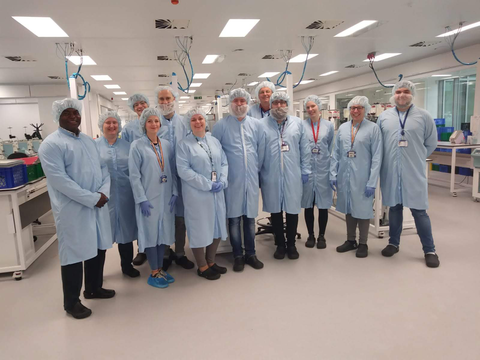 Biomedical science staff from Edinburgh pose for a group photo while wearing hair covers and overcoats. 