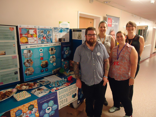 Biomedical scientists pose in front of their stand promoting biomedical science day. 
